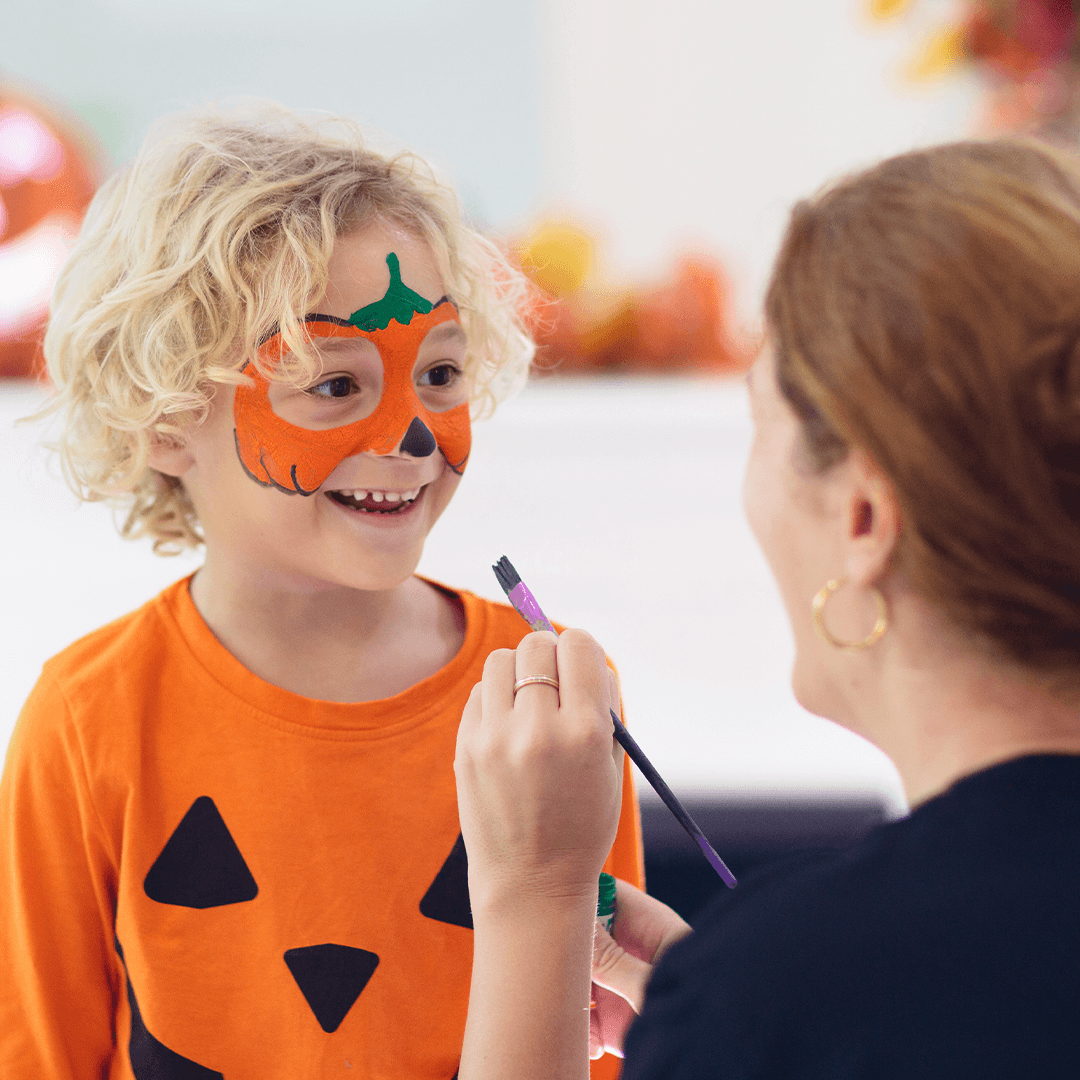 Mamma målar en pumpa på pojkens ansikte till halloween